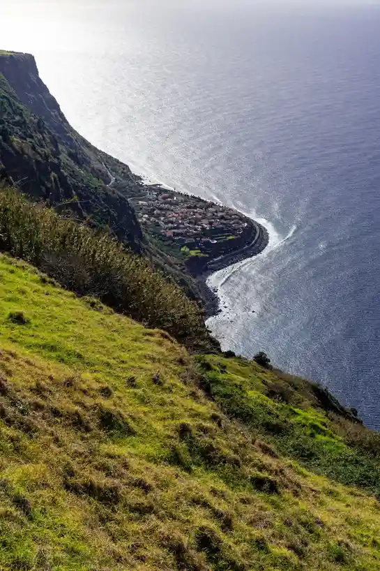 A scenic coastal view shows a small village nestled on a cliffside overlooking the ocean, with a winding road along the…