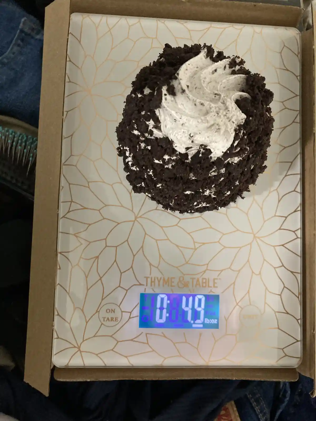 A single chocolate cupcake with white frosting sits on a 'Thyme & Table' digital kitchen scale, which displays the weight…