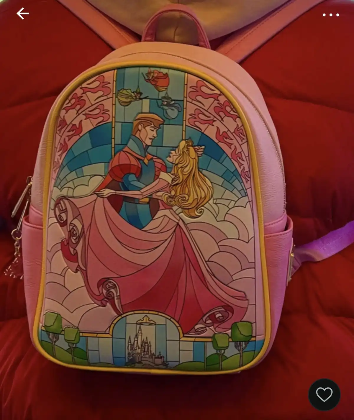 A pink backpack with a stained-glass style design featuring Disney's Aurora and Prince Phillip dancing, with a castle in the…
