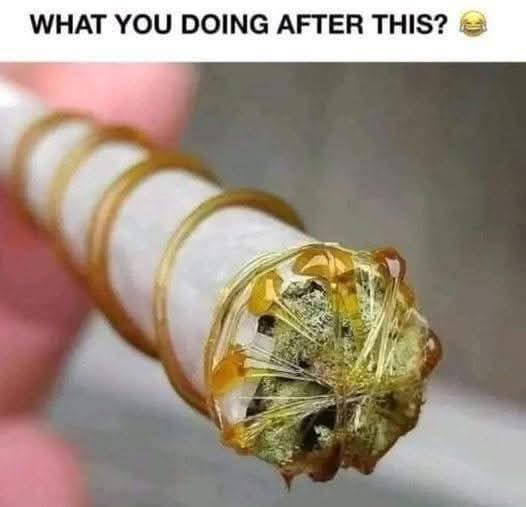 A close-up photo shows a hand holding a cigarette that has been wrapped in multiple golden bands, with the tip covered in a…