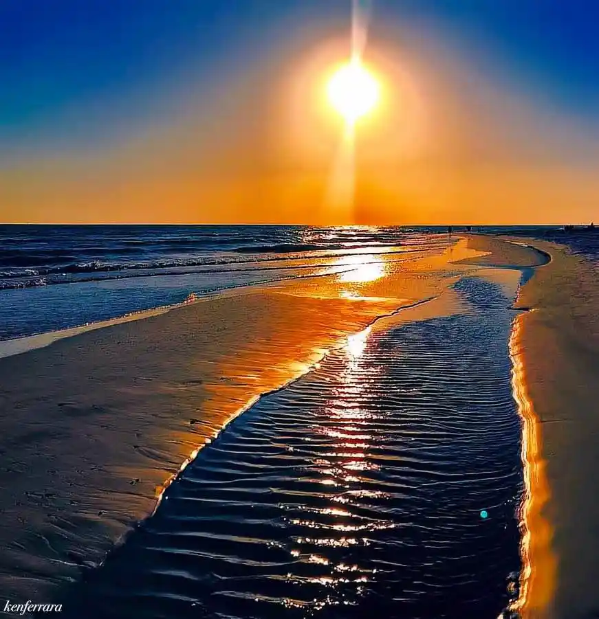 A serene sunset photograph shows the sun low on the horizon over the ocean, its golden light reflecting across wet sand and…