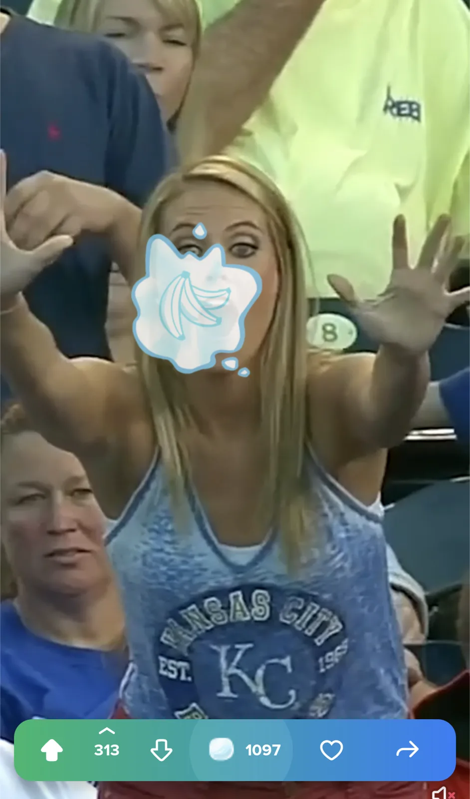 A woman in a Kansas City KC tank top at a sporting event has a banana emoji sticker over her mouth, with her hands raised in…