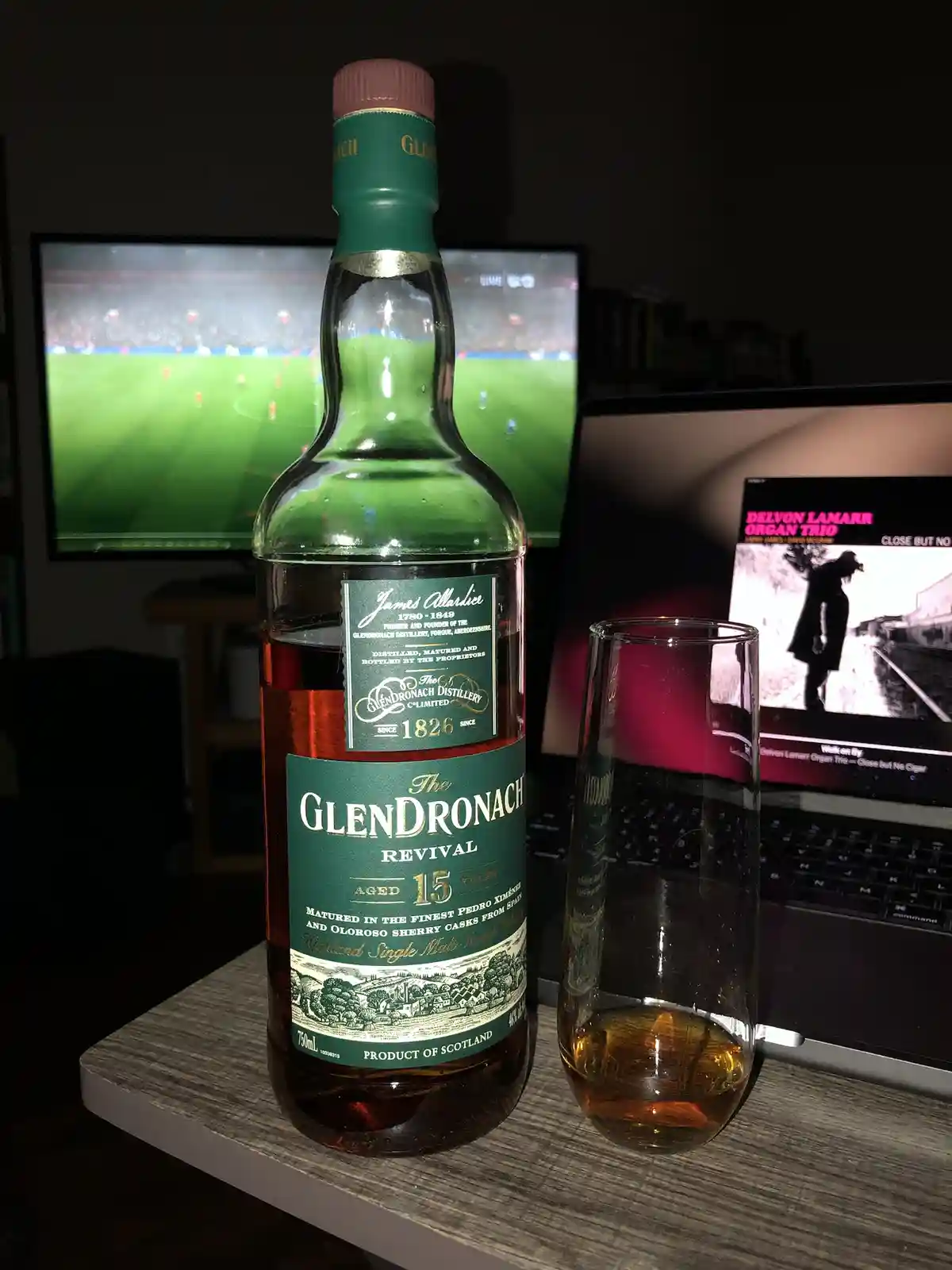 A bottle of Glendronach Revival 15-year-old single malt whisky and a partially filled glass sit on a wooden surface. In the…
