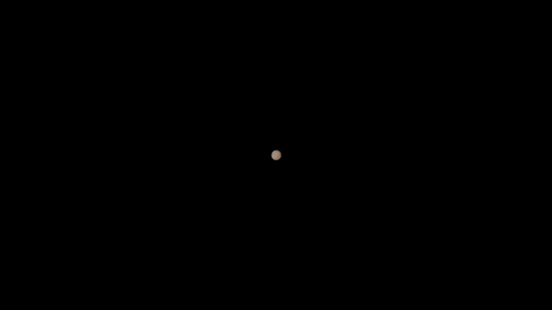 A small, blurry, orange-brown circular object is centered against a completely black background. The overlaid text reads…