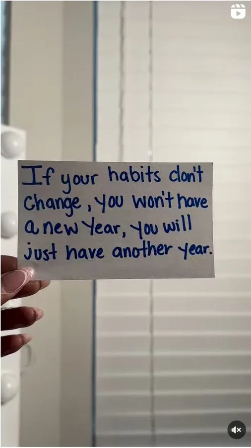 A hand holds a handwritten note that reads 'If your habits don't change, you won't have a new year, you will just have…