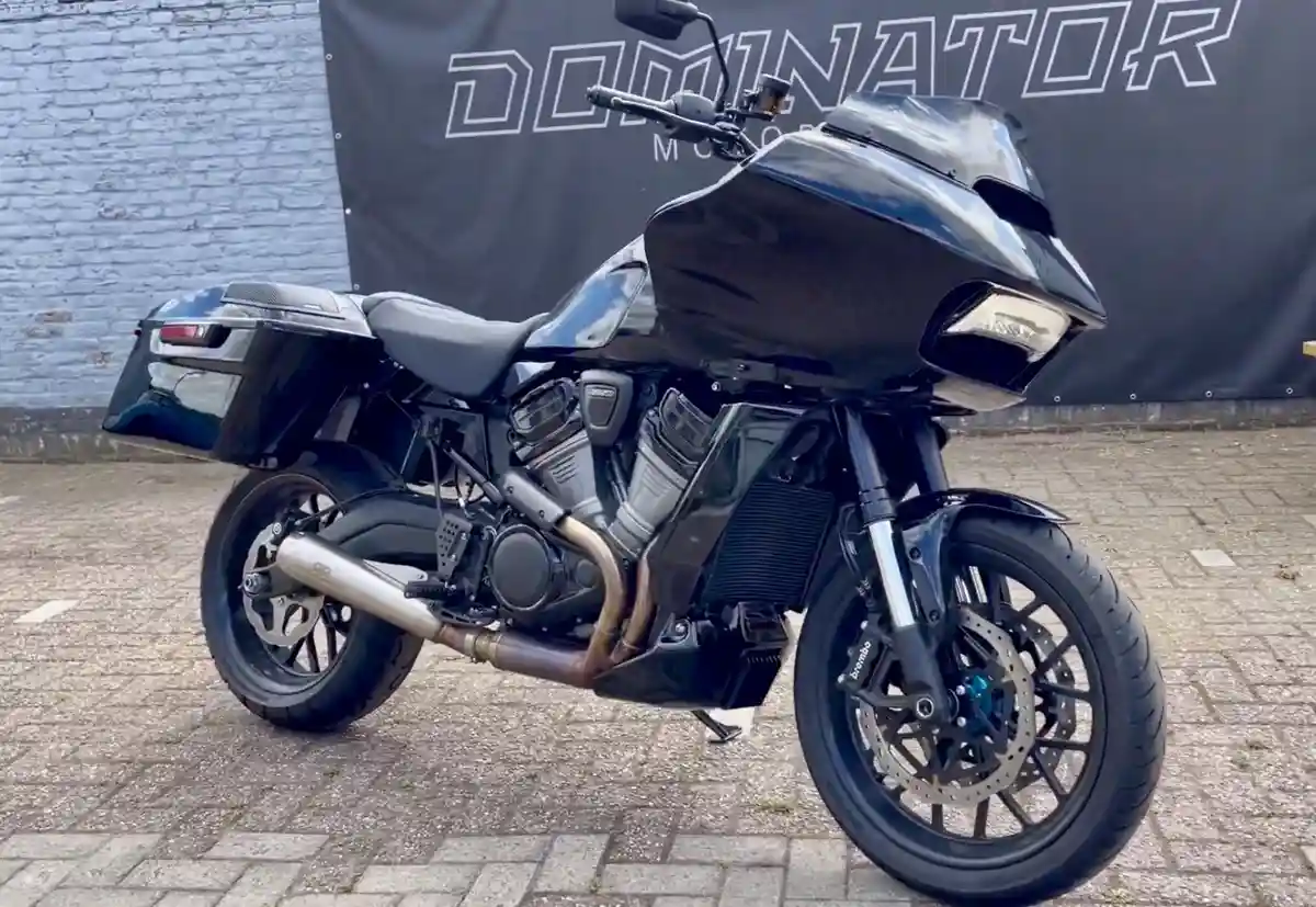 A glossy black touring motorcycle with large fairings, saddlebags, and a prominent exhaust pipe is parked on a paved…