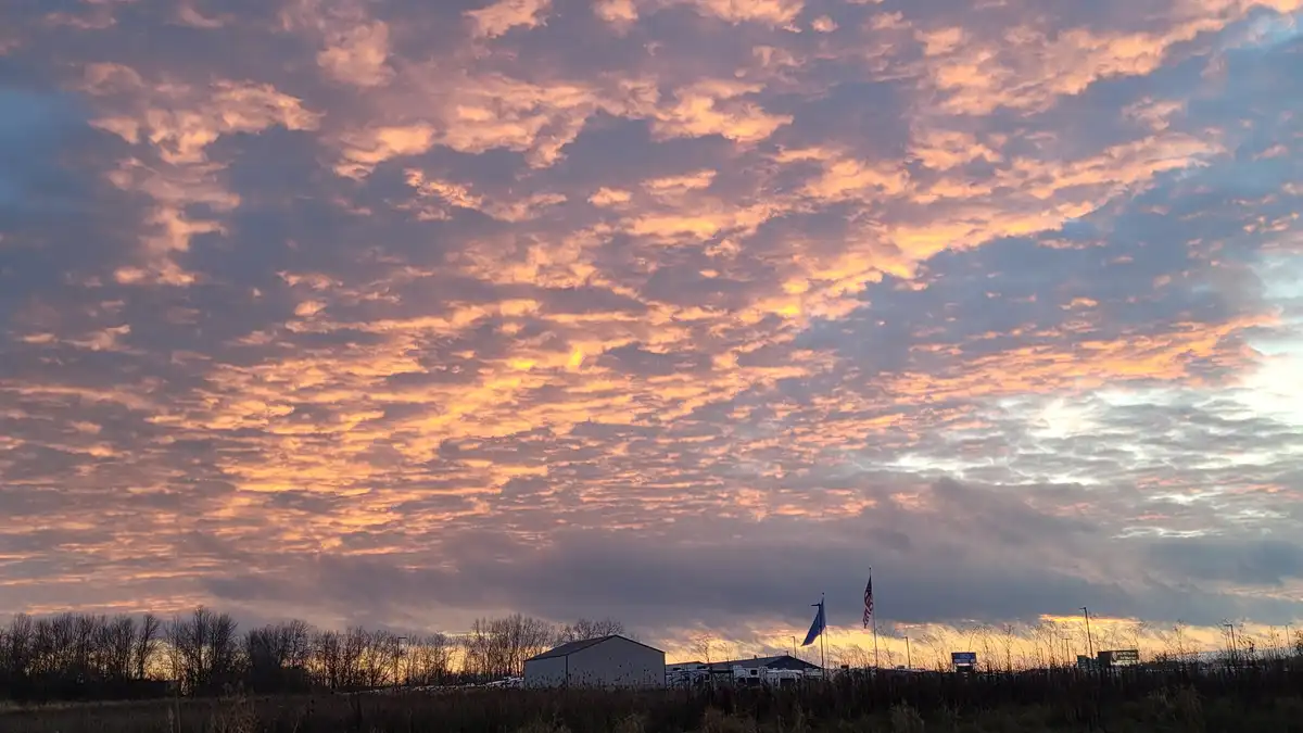 A photograph of a dramatic, colorful sunrise or sunset with orange and purple clouds over a rural landscape featuring a…
