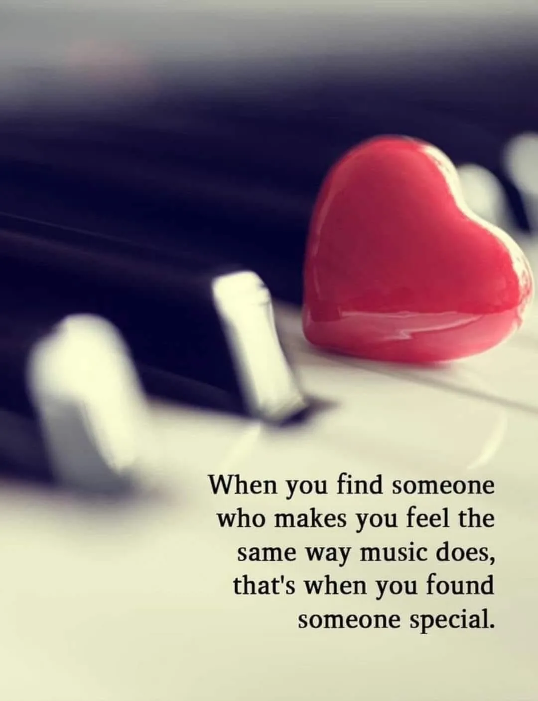 A close-up photo shows a glossy red heart-shaped object resting on the white keys of a piano, with black keys blurred in the…