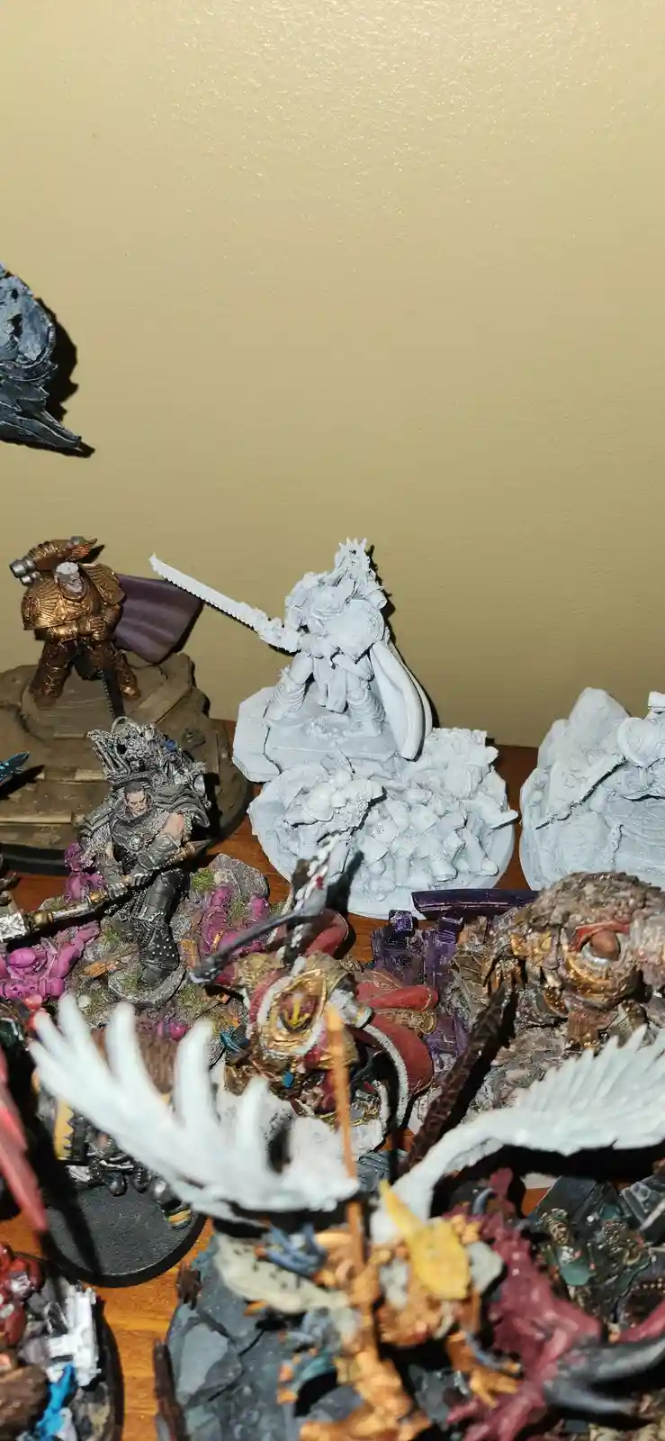 A collection of painted and unpainted fantasy miniatures sits on a wooden surface, with a central unpainted white miniature…