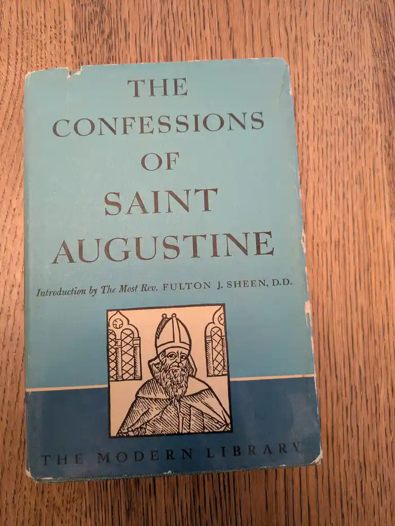 A close-up photo of a vintage blue paperback book titled 'The Confessions of Saint Augustine' with an illustration of a…