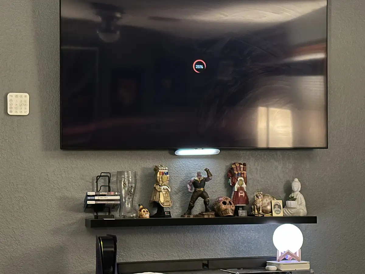 A TV screen displays a red circular progress bar with '25%' inside, mounted above a shelf filled with pop culture…
