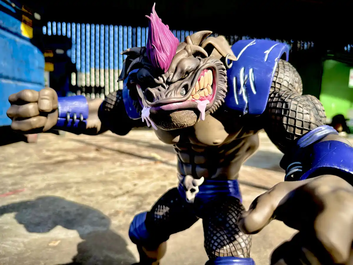 A muscular, monstrous action figure with a pink mohawk, snarling face, and blue armor stands in a fighting stance outdoors…