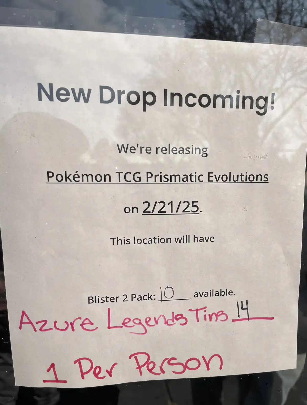 A printed store announcement for a Pokémon TCG product drop is taped to a glass window. The printed text announces a 'New…