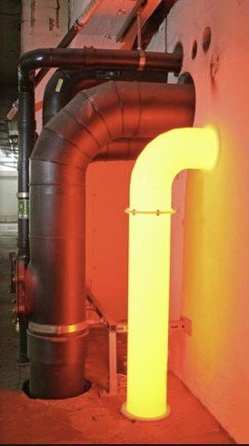 a large industrial pipe, mostly dark and metallic, is shown with one section glowing bright yellow-orange, suggesting…