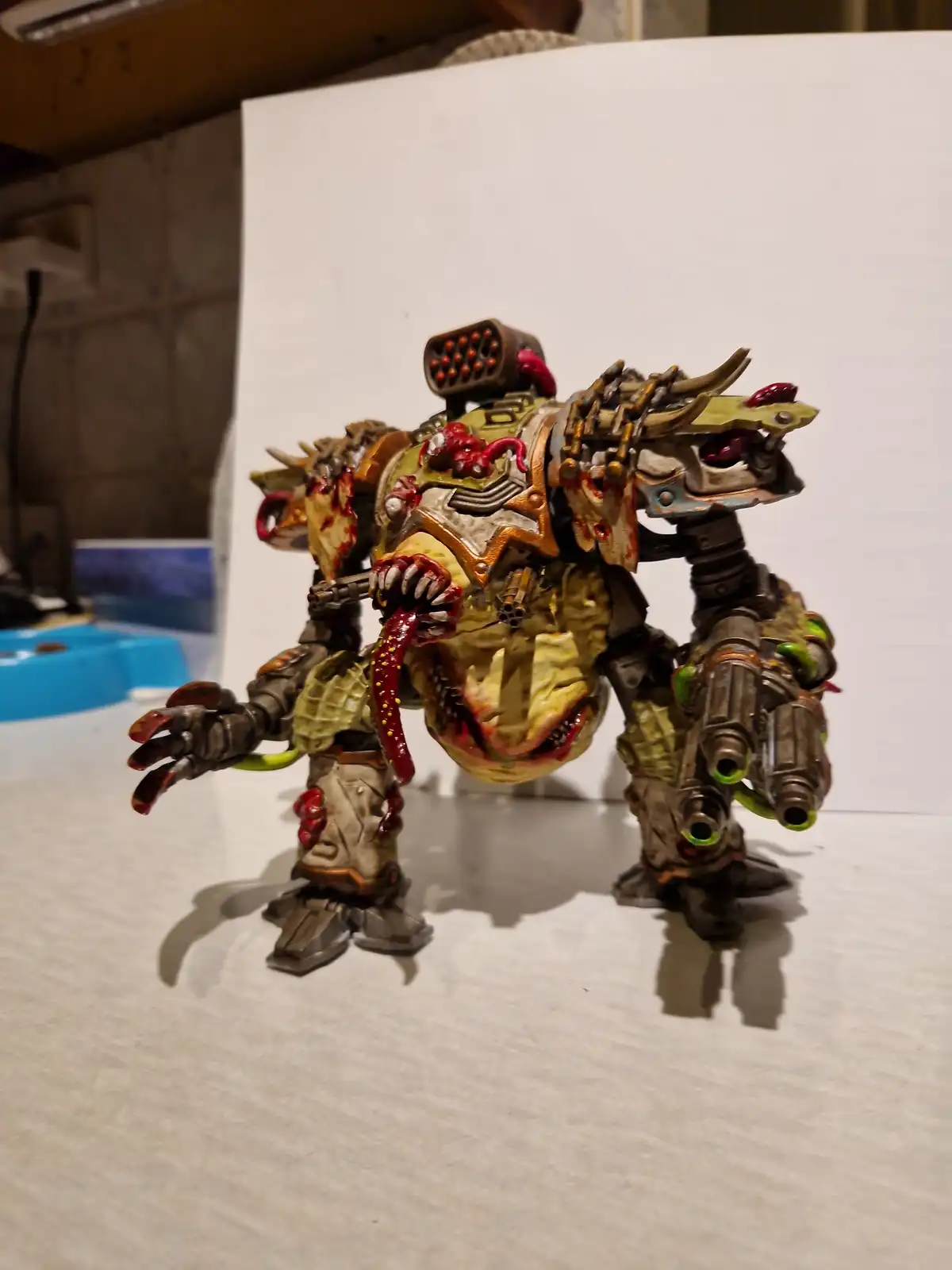 A heavily detailed, grotesque, and blood-splattered miniature of a biomechanical monster with multiple weapons, horns, and…