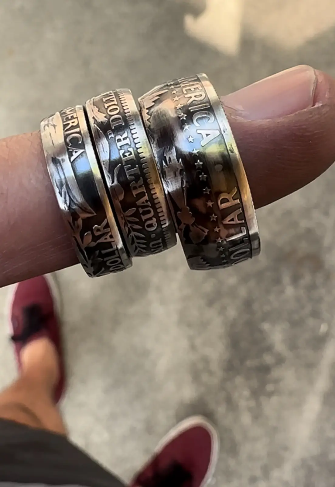 A close-up photo shows three U.S. quarter dollar coins stacked and worn as rings on a person's finger. The coins are visibly…