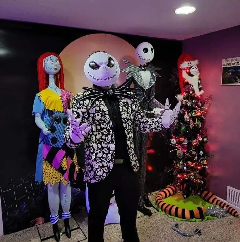 Three people dressed as Jack Skellington, Sally, and Zero from The Nightmare Before Christmas pose in front of a decorated…