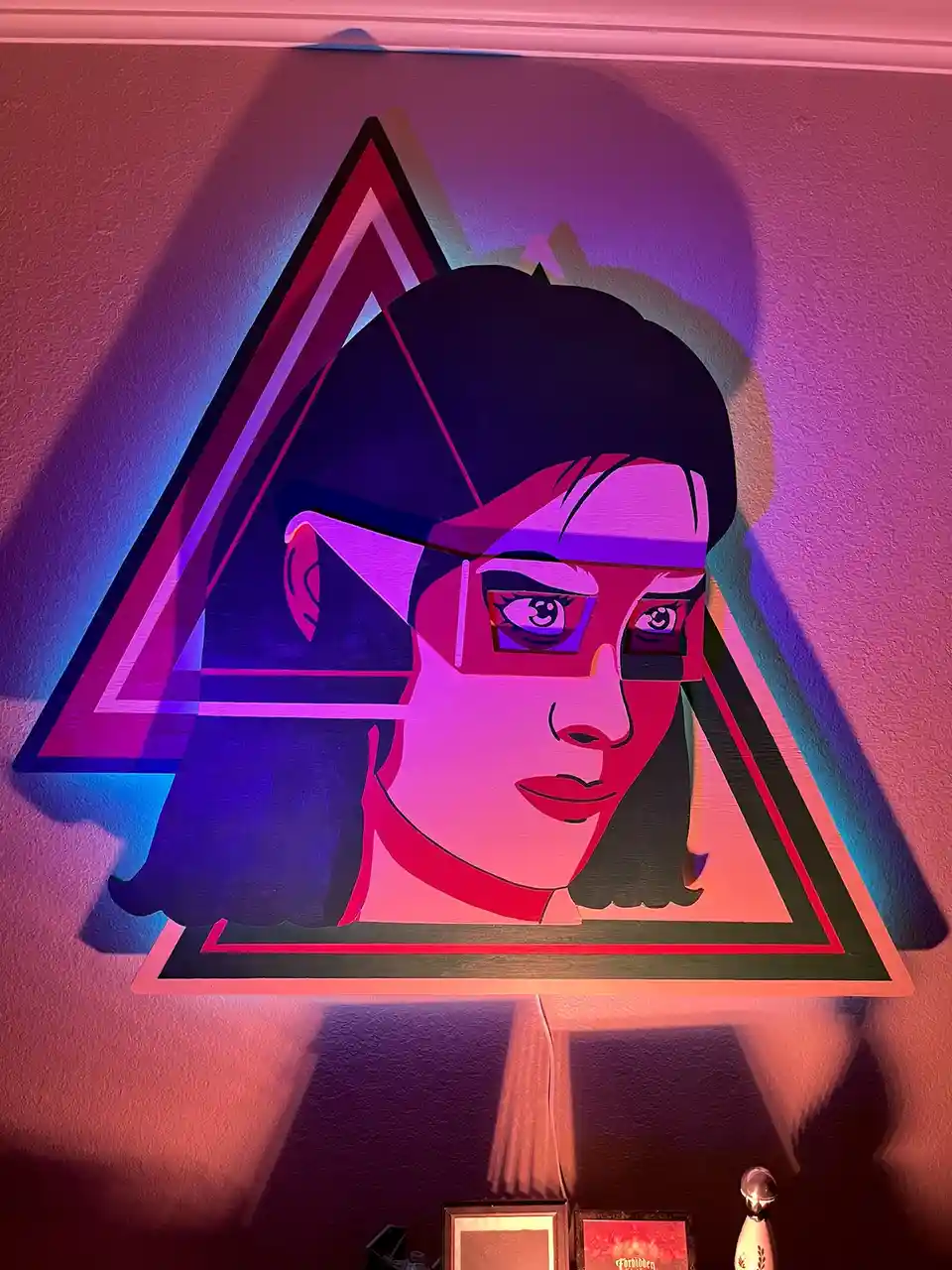A stylized wooden wall art piece depicts a woman's face with glasses, framed within a large, layered triangle. The artwork…