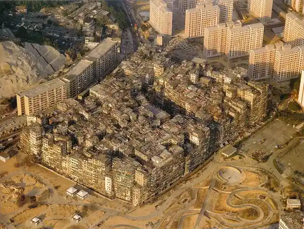 An aerial photo shows a dense, sprawling favela with tightly packed, weathered buildings surrounded by modern high-rise…