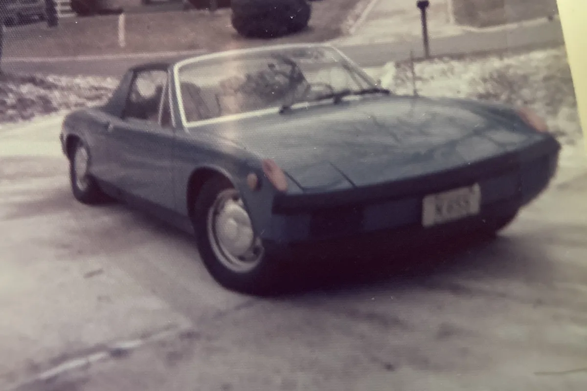 A vintage, slightly blurry photograph shows a blue 1970 Porsche 914 parked on a snowy street, with snowbanks visible along…
