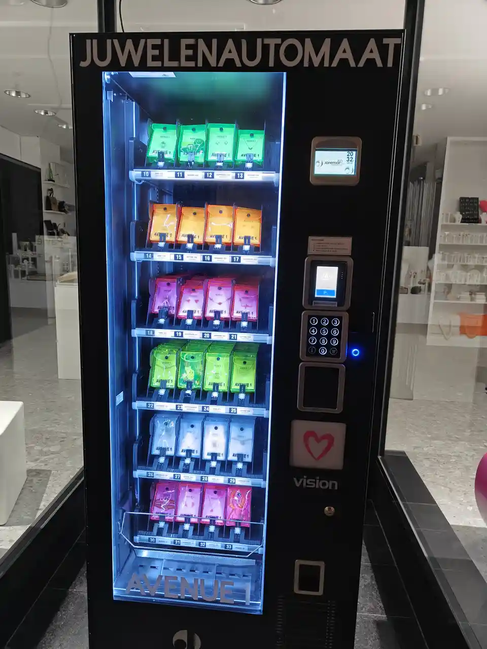 A black vending machine labeled 'JUWELAUTOMAAT' (jewelry vending machine) displays colorful packaged jewelry items on…