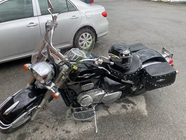 A black cruiser motorcycle with chrome accents and a black helmet resting on the seat is parked next to a silver sedan in a…