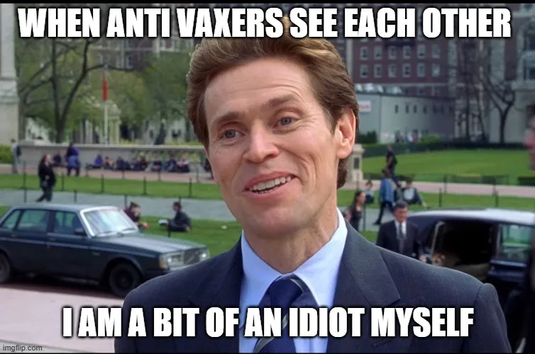A man in a suit and tie smiles awkwardly at the camera, with cars and people in the background. The text overlaid on the…