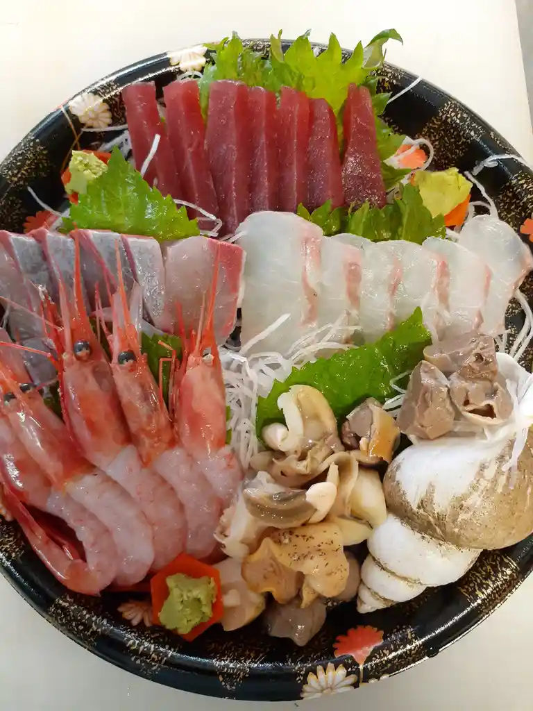 a black ceramic plate with a floral pattern holds an assortment of raw seafood including red tuna slices, pink shrimp with…