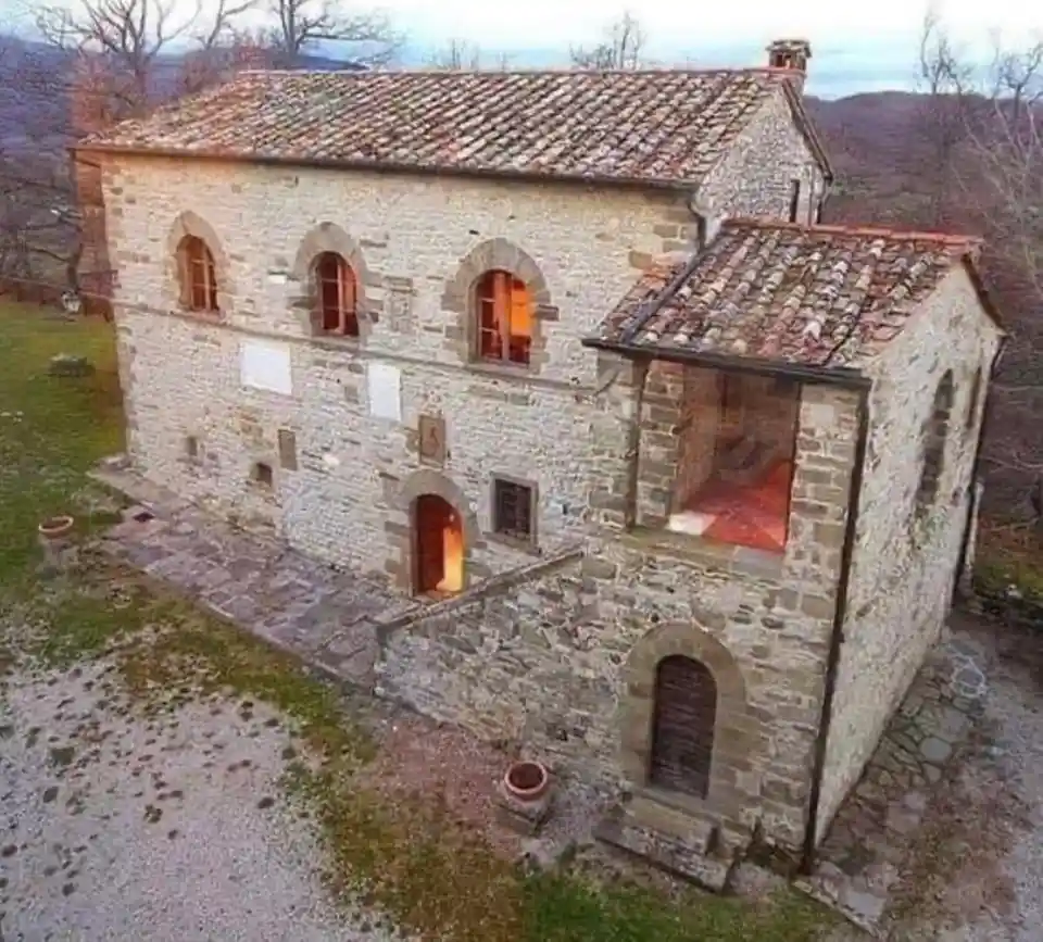 an aerial view of a rustic stone house with a tiled roof, set in a rural landscape with bare trees and hills in the…