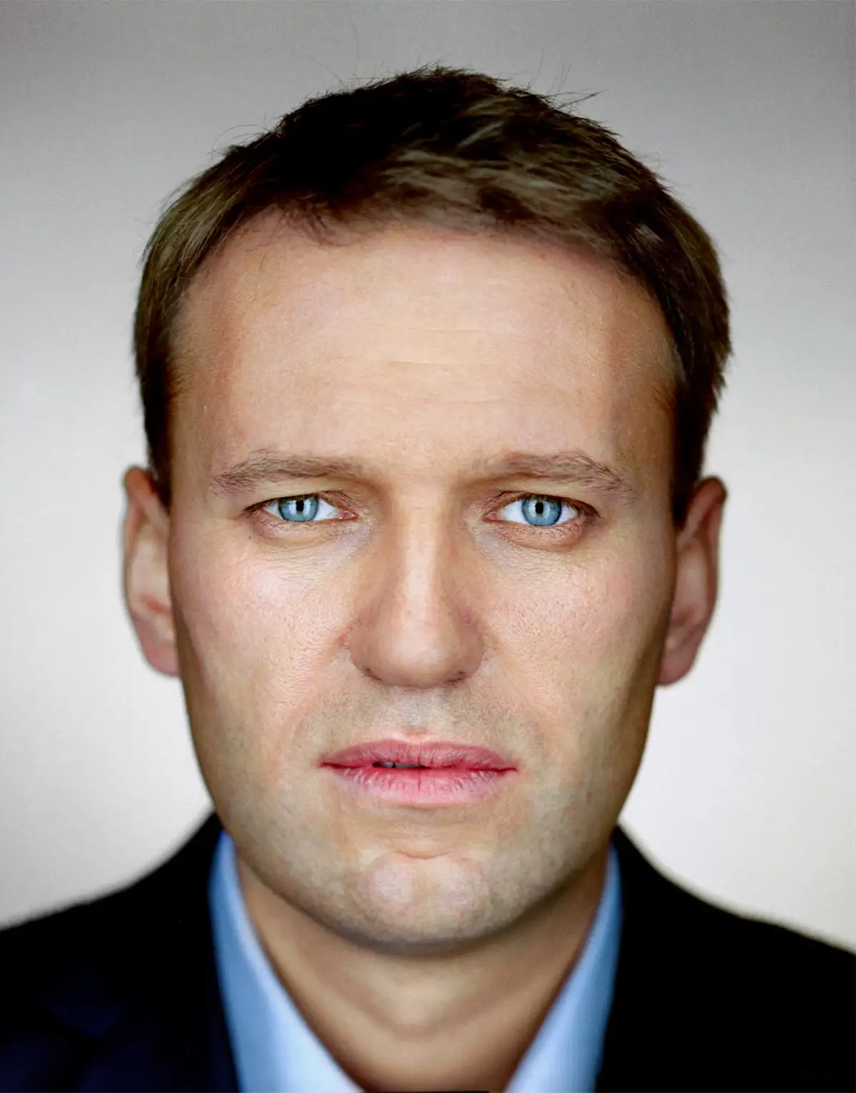 A close-up portrait of a man with intense blue eyes and a serious expression, wearing a dark suit and light blue shirt…
