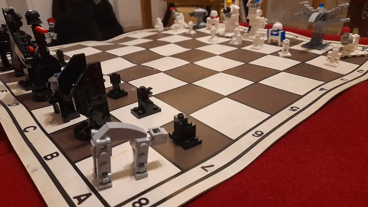 A chessboard with custom-built Lego pieces representing Star Wars characters and vehicles, including a black Darth…