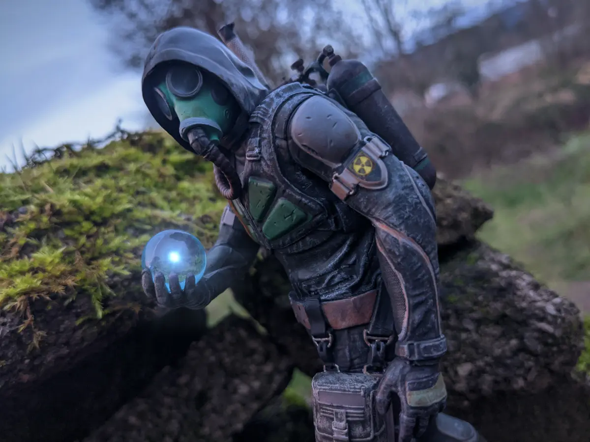A figurine of a person in a green gas mask and bulky, weathered hazmat suit with a radiation symbol on the arm, crouching…