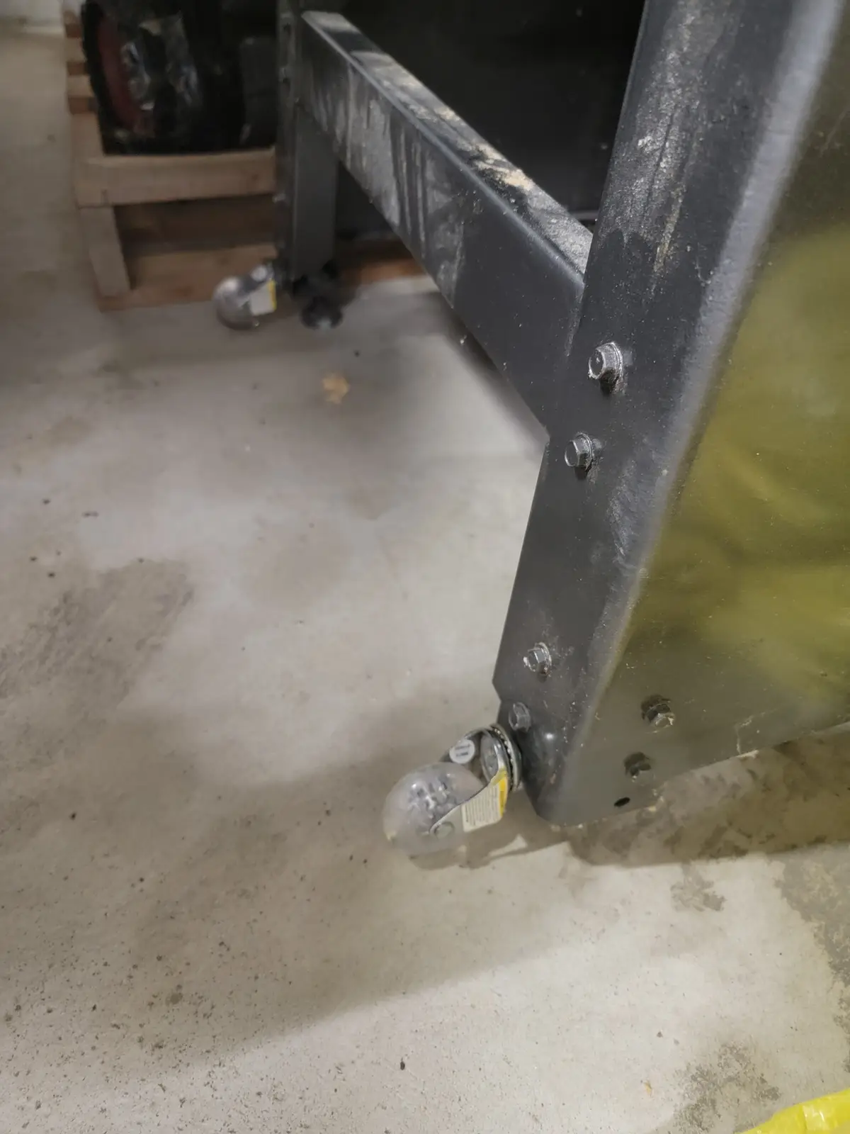 A close-up photo of a metal cart's caster wheel on a concrete floor, with visible bolts and a yellow tag. The overlaid text…