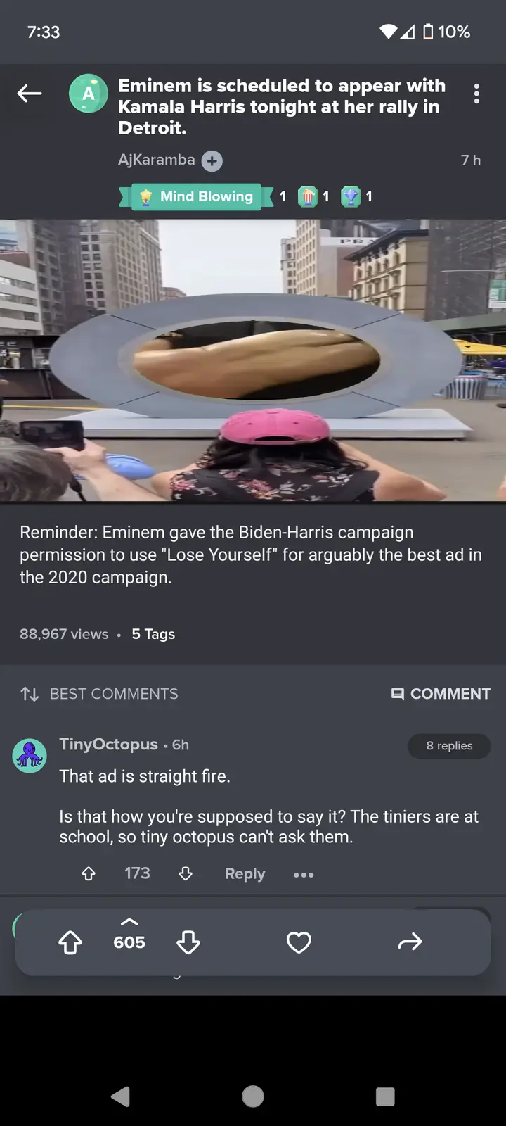 A screenshot of a social media post showing a video of a large public sculpture with a person in a pink hat watching it. The…