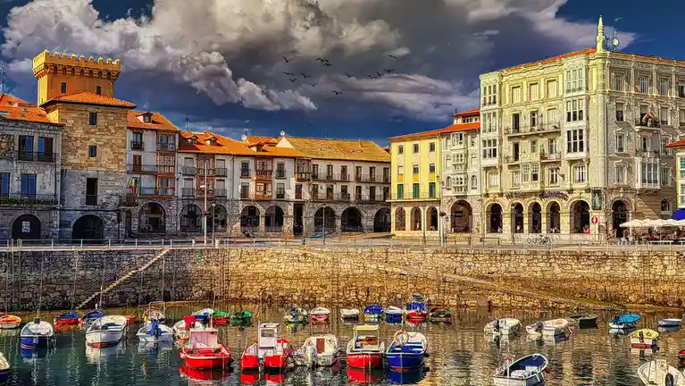 A vibrant, heavily saturated photo of a European harbor with colorful boats docked in front of ornate, multi-story buildings…
