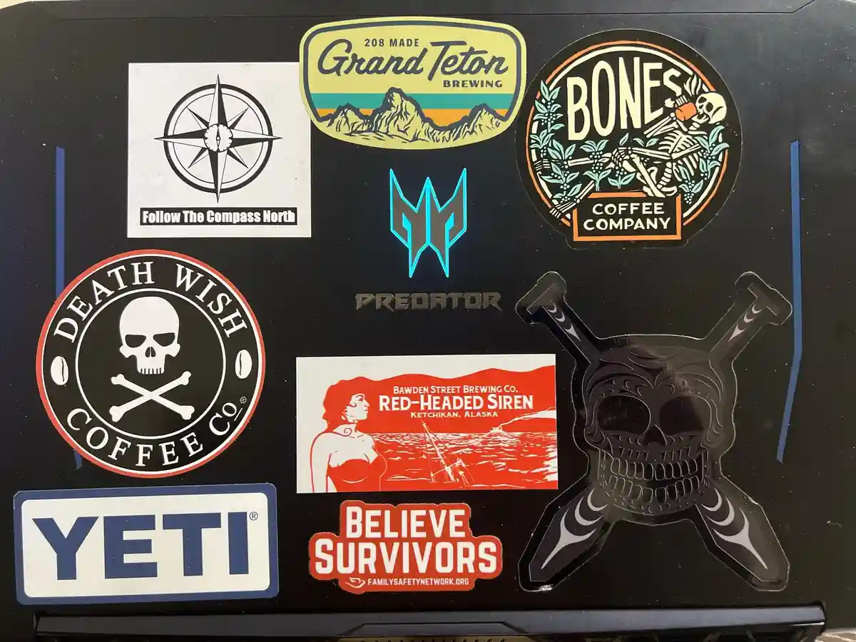 A collection of stickers on a black surface, including 'Death Wish Coffee Co.' with a skull and crossbones, 'Bones Coffee…