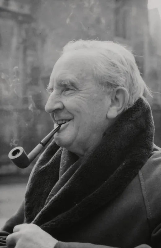 A black-and-white photo of an elderly man with white hair, smiling while smoking a pipe. He wears a dark coat with a thick…