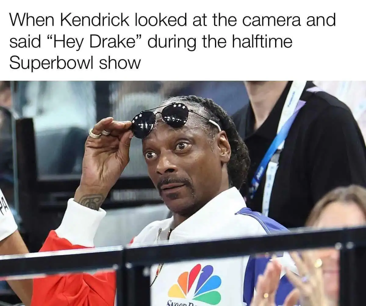A man with braided hair and a white and blue jacket is holding up a pair of black sunglasses with star patterns on the…