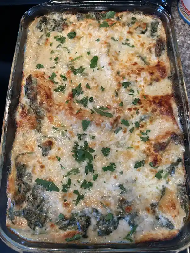 A close-up photo shows a rectangular glass baking dish filled with a cheesy, baked dish topped with melted cheese and…
