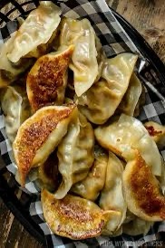 A close-up photo shows a basket filled with golden-brown, crispy-bottomed potstickers or dumplings, resting on a…