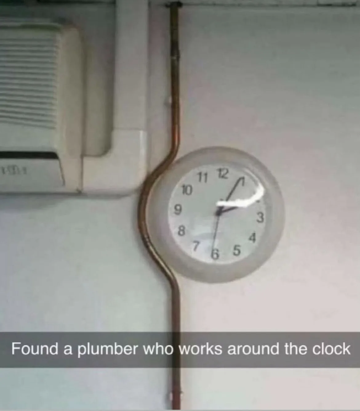 A close-up photo shows a round analog clock mounted on a wall, with a copper plumbing pipe running vertically through its…