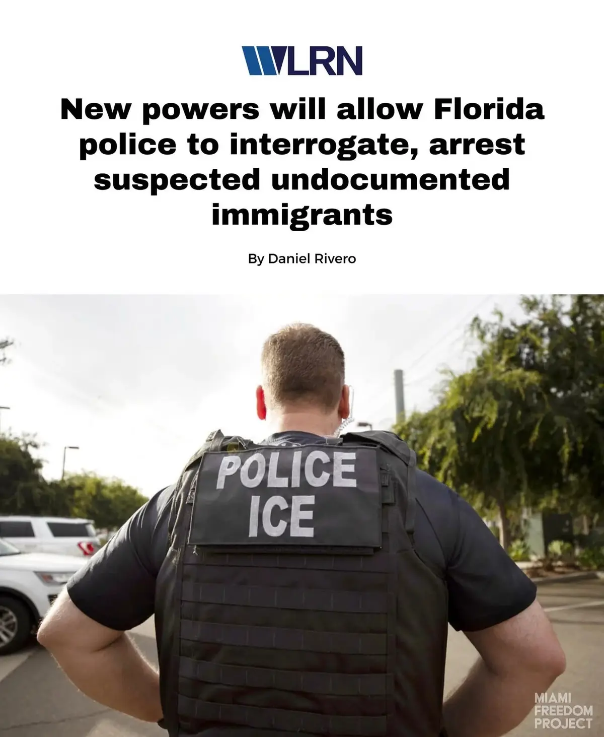 A police officer is shown from behind wearing a tactical vest with 'POLICE ICE' written on it, standing outdoors. The image…