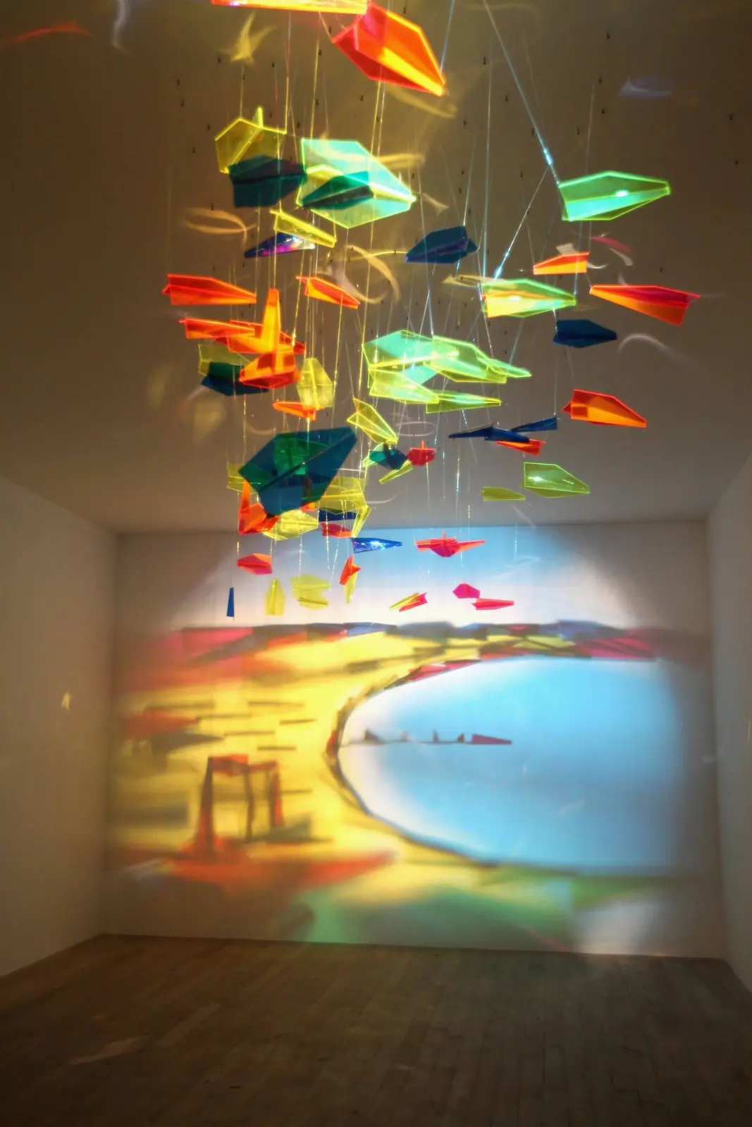 A photo of a colorful, abstract art installation featuring numerous translucent, geometric paper-like shapes suspended from…