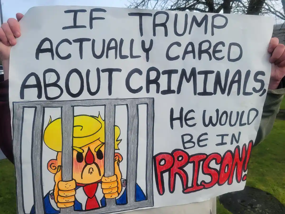 A person holds a handmade protest sign with bold black and red text. The sign reads 'IF TRUMP ACTUALLY CARED ABOUT…