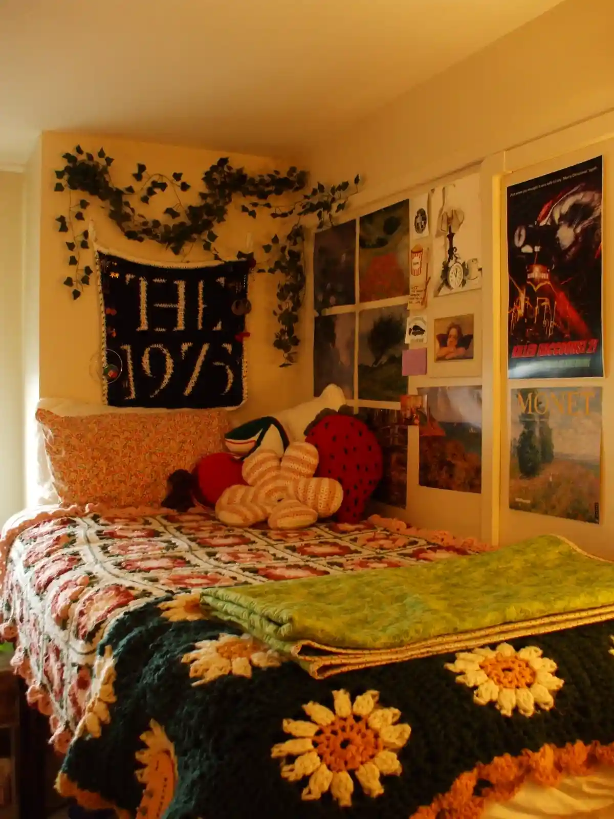 A cozy bedroom features a bed with colorful crocheted blankets and pillows, including a strawberry-shaped one. The wall…