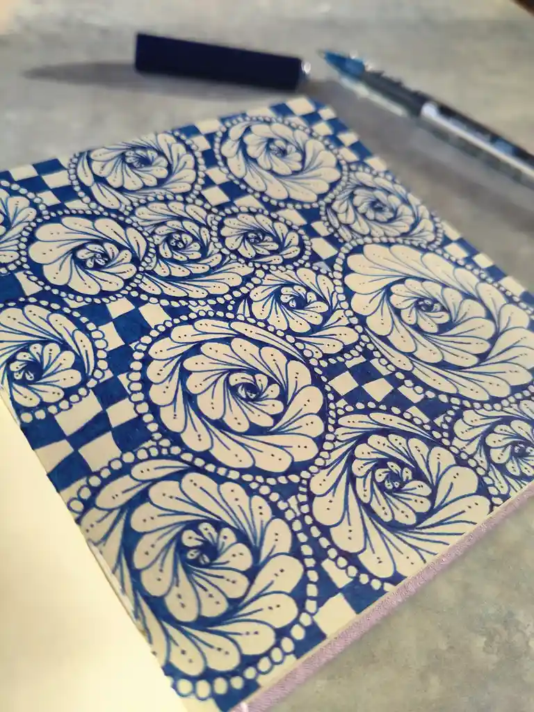 A close-up photo shows a notebook cover decorated with intricate, swirling blue and white floral patterns, resembling a…