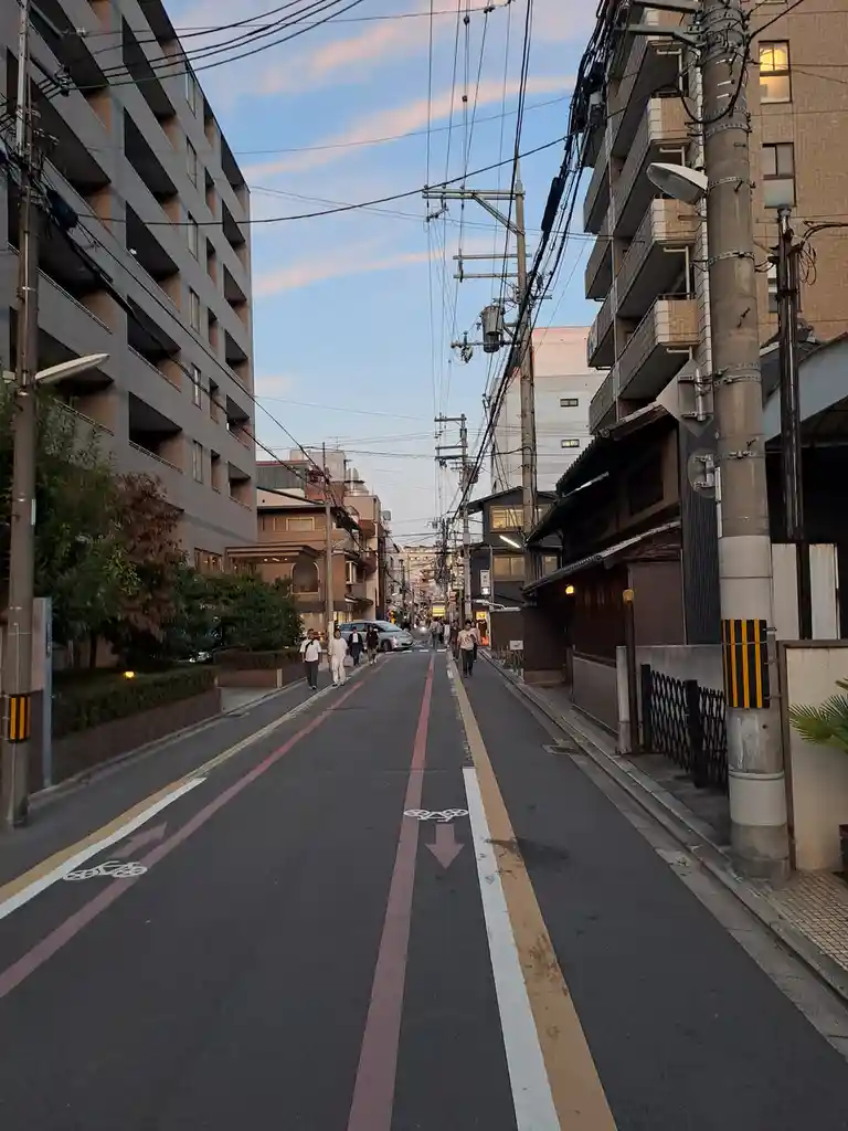 a photo of a narrow urban street in japan, flanked by multi-story buildings and dense overhead power lines against a…