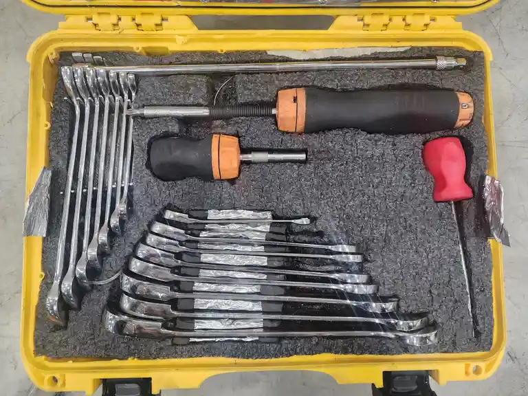 A yellow tool case with black foam insert contains various tools, including wrenches, screwdrivers, and a long rod. Some…