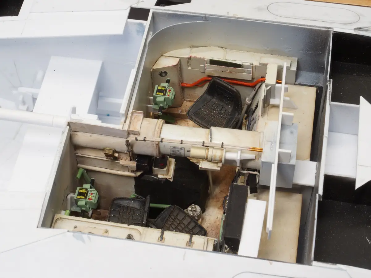 A close-up photo shows the interior of a detailed scale model of a military vehicle, likely a tank, with visible seats…