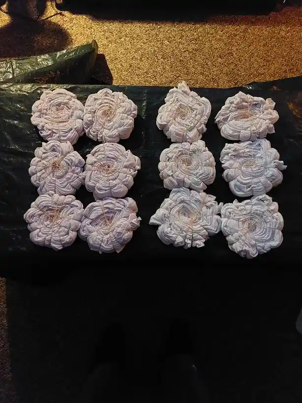 Ten white t-shirts are tightly bound in spiral patterns with rubber bands and arranged in two rows of five on a black tarp…